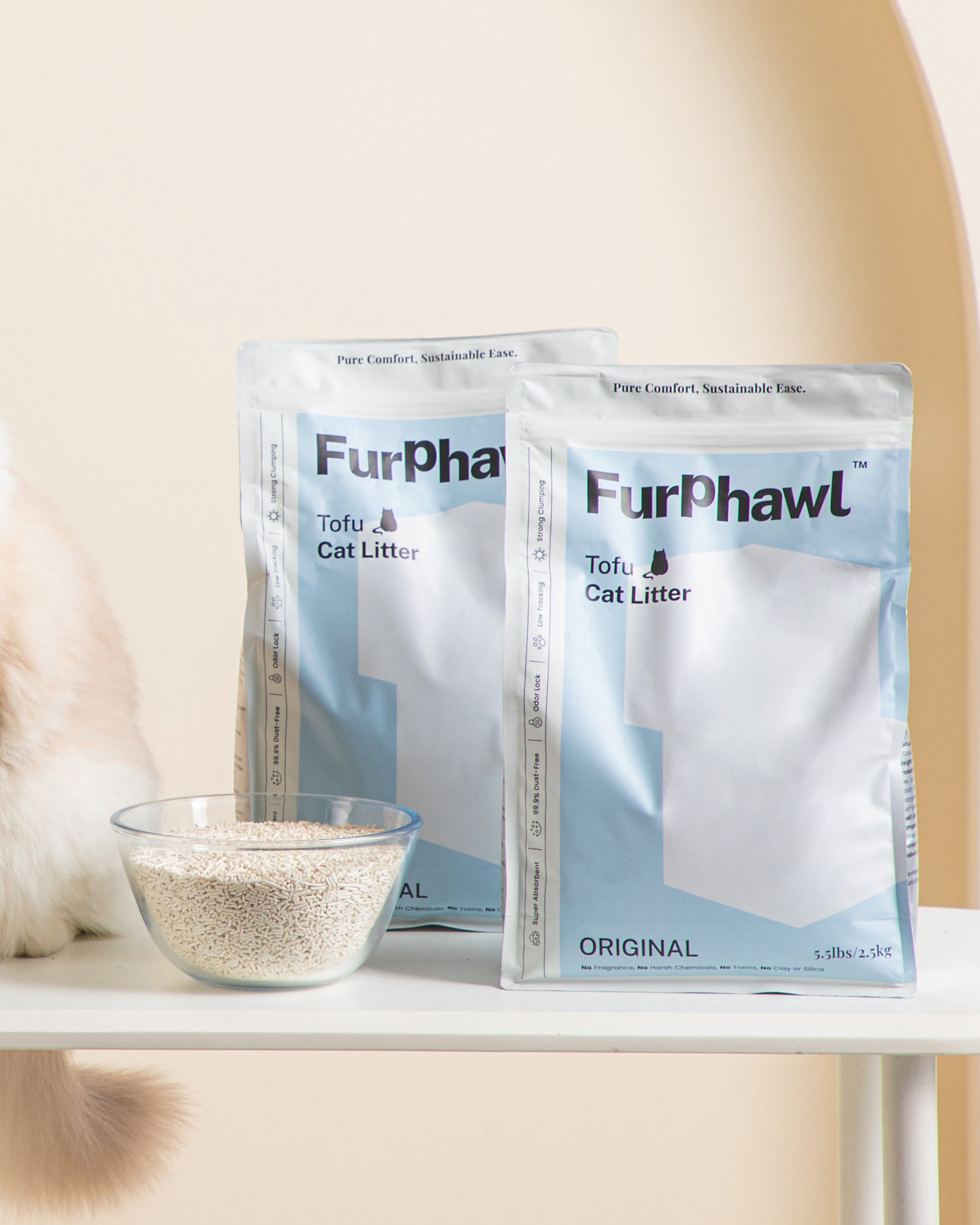 Cat sitting on a table with Furphawl Tofu cat litter packages and a bowl of litter in the background.